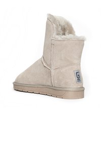 Stivale alla caviglia beige in suede con una morbida fodera in pelliccia, dotato di una patch logo grigia, suola piatta in gomma e dettagli cuciti.