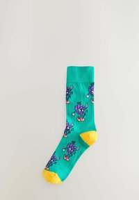 Türkise Socken mit gelbem Zehen- und Bündchenbereich. Mit lustigen Traubenfiguren und Noten, die über die Oberfläche gedruckt sind. Aus einer Baumwollmischung gefertigt.