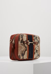 Una borsa rettangolare con corpo in suede marrone, dettagli in stampa serpente e strisce blu scuro, con accessori dorati e chiusura con zip.