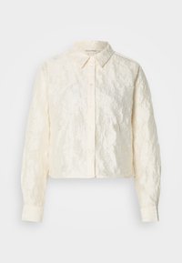 Kremowa koszula o skróconym kroju z fakturowanego materiału, zapinana na guziki z przodu, z długimi rękawami. Posiada klasyczny kołnierzyk i lekko pomarszczony wygląd.