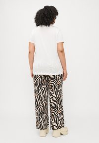 Camasa albă cu mânecă scurtă asortată cu pantaloni largi cu un model de dungi zebra în culori negre și maronii. Modelul poartă saboți de culoare deschisă.