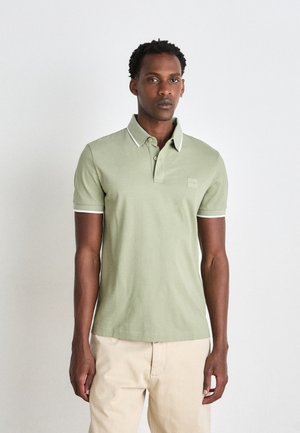 Light green polo shirt with a contrasting white collar and sleeve trim, featuring a small logo patch on the chest, paired with beige pants.