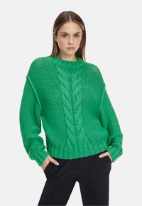 Grüner gestrickter Pullover mit Kabelstrickmuster, geripptem Halsausschnitt und Bündchen. Lockerer Schnitt mit überschnittenen Schultern und strukturiertem Stoff.