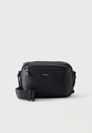 Sac bandoulière en cuir noir avec poche zippée à l'avant et sangle en tissu réglable, marqué du logo "BOSS" sur le devant.