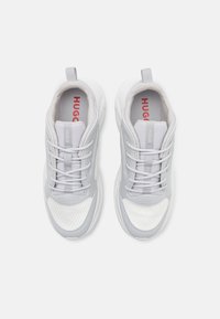 Szare buty sportowe z siateczki i materiału syntetycznego. Posiadają sznurowadła, wyściełany kołnierz i czerwony logo "HUGO" na wkładce.