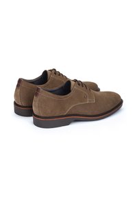 Chaussures en suede marron avec une finition lisse, un bout rond et un système de laçage. Présentent une bande orange contrastante sur la semelle et un talon marron uni.