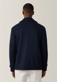 Chaqueta de mezcla de lana en color navy con un gran cuello, costuras visibles y puños abotonados. Diseñada con una forma ajustada y entallada.