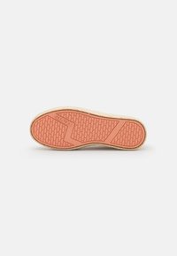 Semelle de chaussure avec une surface en caoutchouc rose texturé ; présente un motif en chevrons et un logo en relief. Les bords sont finis en beige clair.