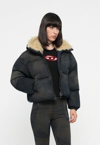 Pufferjack in donkere tinten met een faux fur-gevoerde capuchon, voorzien van een rits en een oversized silhouet. Zwarte fitted broek met ritsdetails.