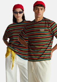 Pruhovaná trička v červené, žluté, modré a černé barvě s krátkými rukávy. Design obsahuje logo "Stranger Things".