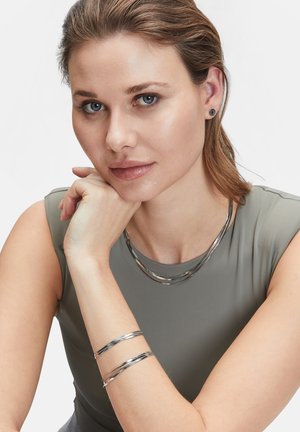Zilveren metalen sieraden met een stijlvolle, gelaagde ketting en een bijpassende armbandenset, tentoongesteld op een model tegen een effen achtergrond.