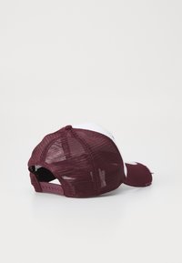 Bordeauxrot und weiße Baseballmütze mit Netzrücken, gebogenem Schirm und Druckverschluss. Sie hat einen used-Look und ein Stofflogo-Detail auf der Vorderseite.