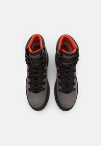 Harmaat vaelluskengät mustilla yksityiskohdilla ja oranssilla vuorauksella. Ominaisuuksiin kuuluu tekstuuripintainen nahkavarsi, mustat nauhat punaisilla ompeleilla ja kestävä pohja.