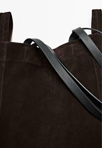 Brun ruskinds taske med to mørke læderremme. Har synlig syning på overfladen af ruskindet. Simpelt design uden yderligere udsmykninger.