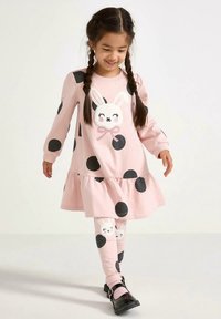 Rochie roz cu buline negre, tiv cu volane și o aplicație cu iepuraș. Colanții asortați au un model similar și detalii cu iepuraș.