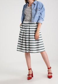 Jeansjacka över en randig t-shirt, i kombination med en knälång grön och vit randig kjol och röda blockklackskor.