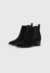 Black suede ankle boots with a low heel, featuring a rounded toe and elastic side panels, placed against a white background.