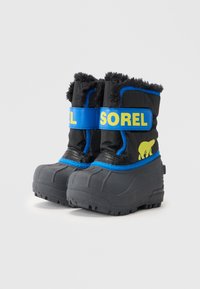 Fekete szigetelt csizmák szürke gumitalppal, kék kiegészítőkkel és sárga "SOREL" logóval. A tetején műszőrme díszítéssel.