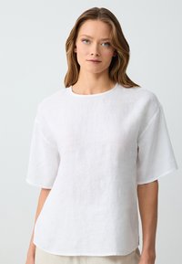 Camicia bianca in lino con scollatura tonda e maniche corte e larghe. Tessuto liscio, vestibilità morbida e spacco laterale all'orlo.