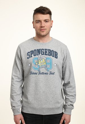 Mand iført grå sweatshirt med Svampebob Firkant, der holder en baseballbat, tekst "SPONGEBOB 99 Bikini Bottom's Best."