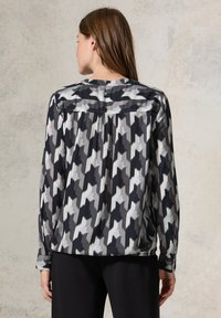 Blusa a maniche lunghe in tessuto leggero con un motivo a zigzag in nero, bianco e grigio; presenta un polsino con bottone e un retro plissettato.