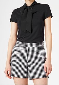 Black short-sleeve top with a bow tie collar paired with high-waisted black and white gingham check shorts. Smooth texture and tailored fit.