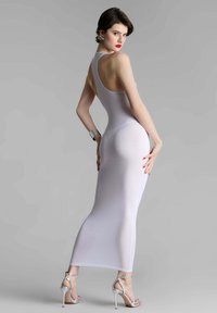 Weißes, figurbetontes Kleid mit hohem Ausschnitt und offenem Rücken, aus durchscheinendem Stoff. Kombiniert mit silbernen Stiletto-Heels und einem Armband.