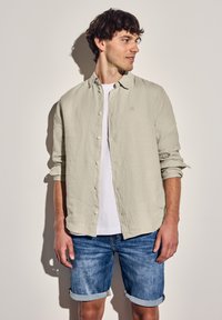 Světle šedá košile s dlouhým rukávem a ohrnutými rukávy, v kombinaci s bílým tričkem a džínovými šortkami. Jednoduchý design, volný střih.