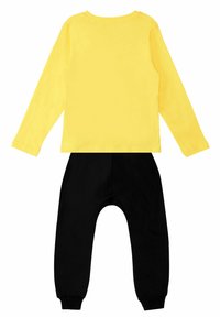 Gelbes Langarmshirt mit Rundhalsausschnitt, kombiniert mit schwarzen Jogginghosen. Weicher Baumwollstoff, lässige Passform und gerippte Bündchen an den Hosen.