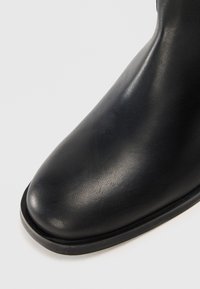 Svart skinn ankelstøvel med rund tå, glatt tekstur, subtil glans og lav gummisåle. Designet er minimalistisk og strømlinjeformet.