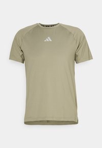 Camiseta atlética de manga corta en verde oliva claro, con cuello redondo y logo de Adidas centrado en el pecho.
