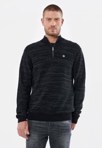 Sweat à zip noir présentant un motif texturé avec des rayures horizontales, accompagné de poignets et d'un ourlet côtelés, ainsi qu'un petit logo sur la poitrine.