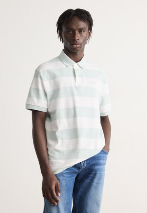 Lys grøn og hvitstripete polo-skjorte med krage, med en liten brodert logo på brystet. Brukt sammen med blå jeans.