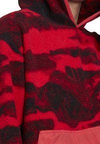 Röd och svart fleece-pullover med huva, med en texturerad yta och en enfärgad rosa ficka fram.