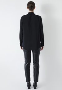 Camicia nera a maniche lunghe realizzata in tessuto leggero, con colletto e vestibilità rilassata, abbinata a pantaloni in pelle nera aderenti.