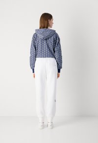 Huvjacka i blått med geometriskt mönster, elastiska manschetter; parat med vita smalrandiga byxor med logodetalj på sidan.