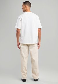 White short-sleeve T-shirt, cotton fabric, relaxed fit, paired with cream-colored pants, detailed stitching, and black shoes.