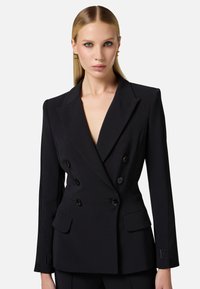 Blazer nero doppiopetto con scollatura a V profonda, spalle strutturate, due ampie tasche frontali e dettagli con bottoni.