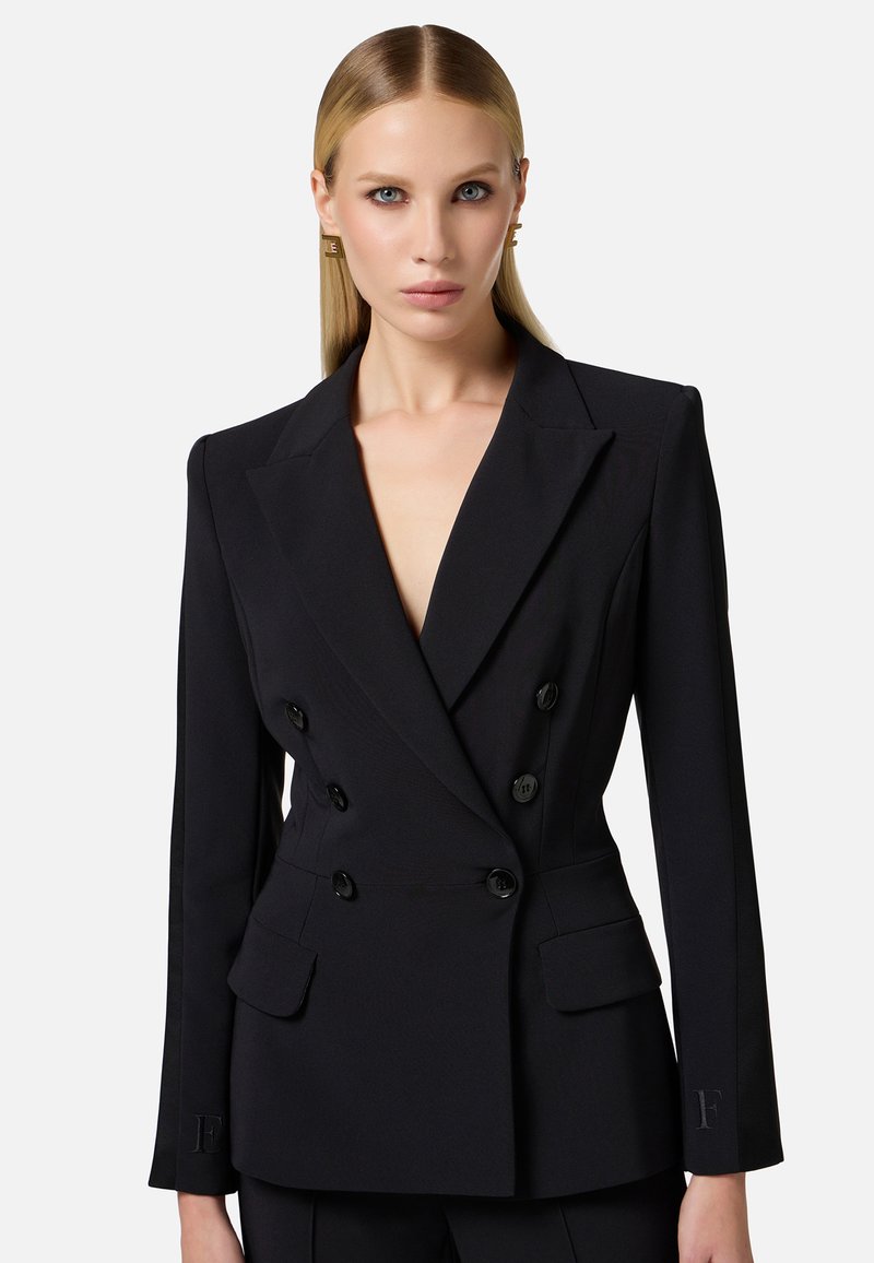 Blazer nero doppiopetto con scollatura a V profonda, spalle strutturate, due ampie tasche frontali e dettagli con bottoni.