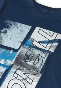 Tela azul marino con un estampado gráfico en bloques blancos, azules y grises que presentan texturas abstractas y letras delineadas en negrita.
