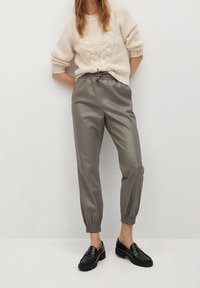 Jasno beżowy sweter w splocie warkoczowym, połączony z jasnoszarymi joggerami z ekoskóry o tapered kroju oraz czarnymi loafersami.