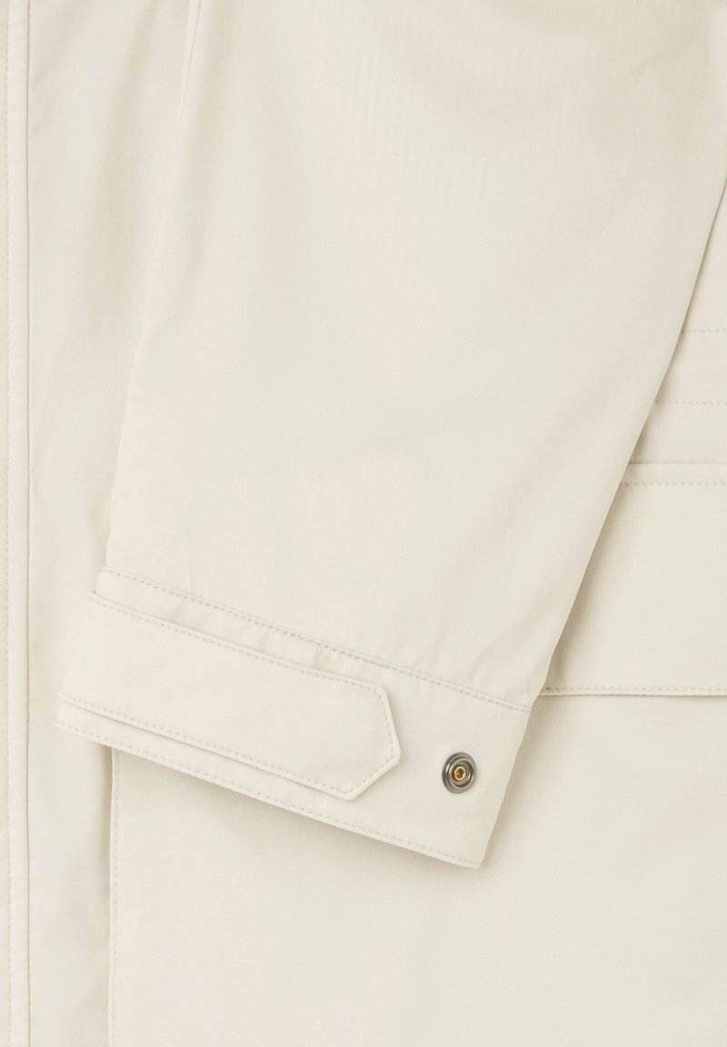 Manche de veste légère couleur crème avec une texture lisse, dotée d'un bouton-pression et d'un onglet pour un ajustement. Détail de couture subtil.