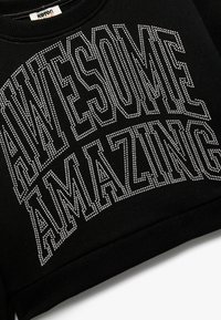 Sudadera negra con las palabras "AWESOME AMAZING" en grandes embellishments de piedras preciosas plateadas. Textura suave con diseño de cuello redondo.