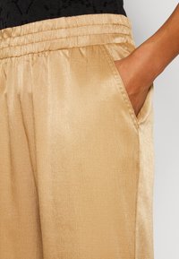 Gouden, geweven stof broek met een elastische tailleband en zijzakken. Glad glanzend oppervlak en een rechte snit. Zichtbare naaddetails bij de zakken.