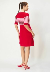 Punainen neulemekko, jossa on raidallinen ribbineule yläosa, lyhyet hihat ja vartalonmyötäinen siluetti. Yhdistettynä punaisiin korkokenkiin.