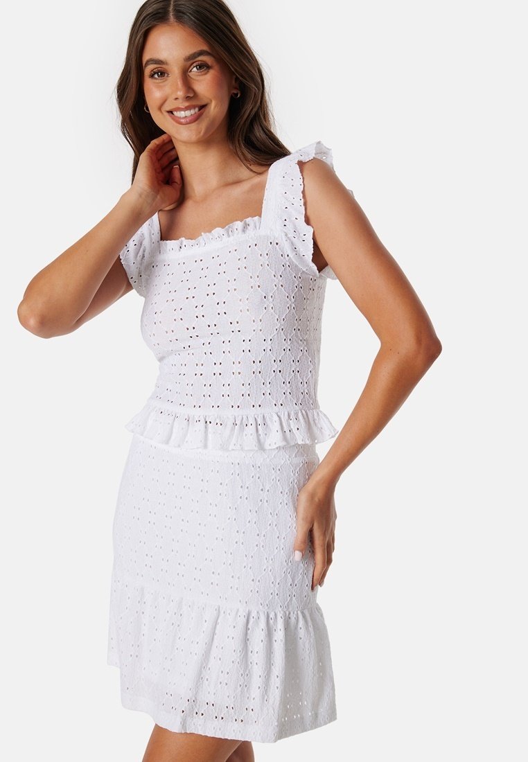 Bílá šaty z krajkového materiálu s čtvercovým výstřihem, volánkovými ramínky, peplum pasem a sukní v patrech. Obsahují jemné výřezy po celém povrchu.