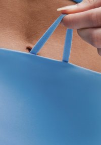 Helles blaues Kleidungsstück mit glatter Textur, das dünne Träger hat, die gezogen werden. Nahaufnahme zeigt minimale Details und keine ausgeprägten Muster.