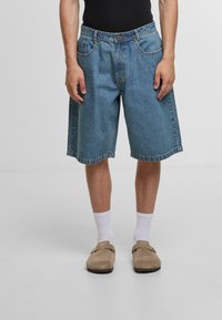 Denimshorts lavet af lyseblå stof, med en l�øs pasform, fem lommer og en mellemhøj talje. Kombineret med hvide strømper og beige fodtøj.