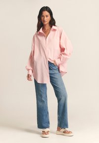 Striped pink button-up shirt with a chest pocket, paired with blue wide-leg jeans and beige platform sandals. Casual fit and oversized design.