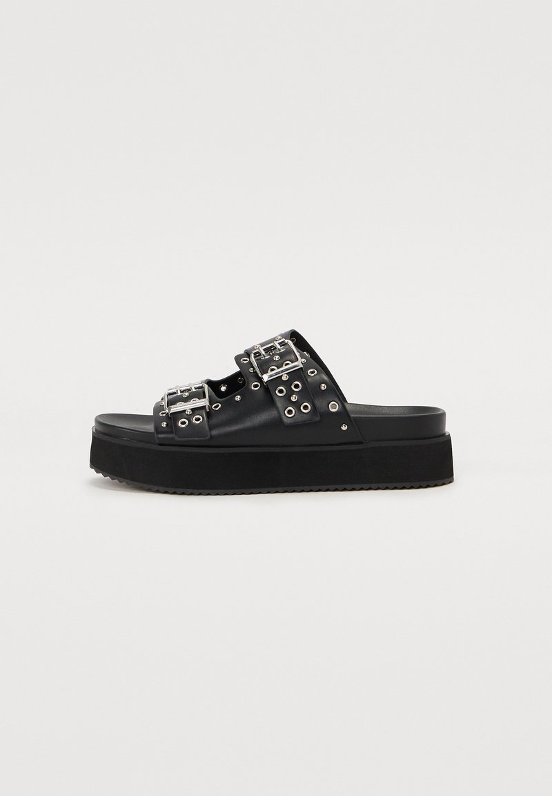 Black platform sandals made of leather with two wide straps featuring silver buckles and decorative metal grommets. Textured sole.